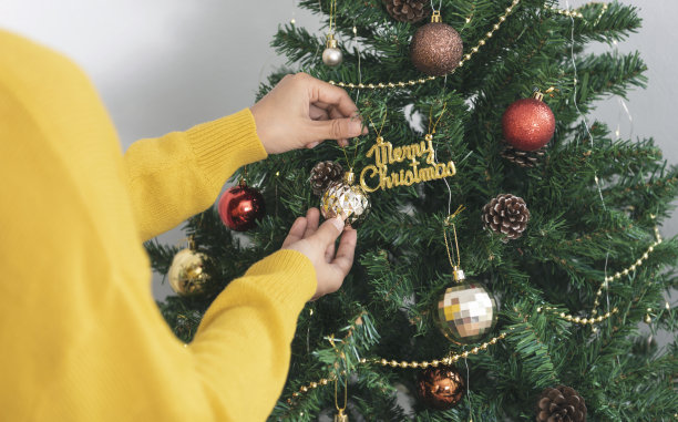 妇女在圣诞节用装饰品装饰圣诞树。图片下载