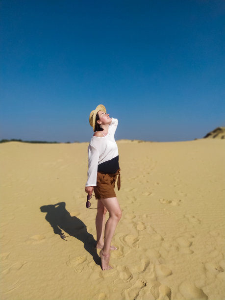 一个穿着白色衬衫和棕色短裤的年轻女子在沙漠中行走图片下载