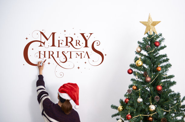 女人在圣诞节装饰圣诞树，在墙上写圣诞快乐的文字。图片下载
