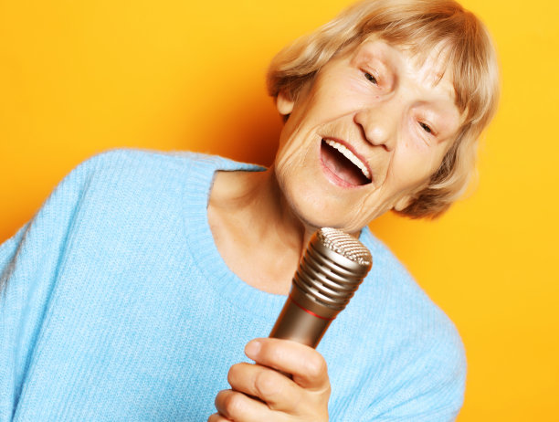 快乐的老女人拿着麦克风唱歌，玩得很开心，在黄色的背景上表现出音乐才能图片下载