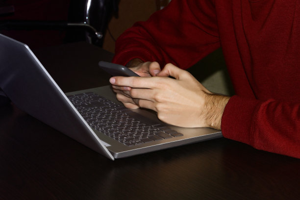 男性手里拿着智能手机。笔记本电脑在桌子上。上班族。图片下载