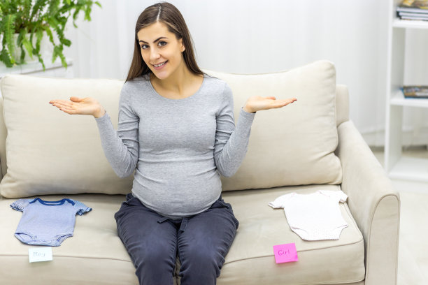 孕妇穿着童装坐在沙发上的照片。图片下载