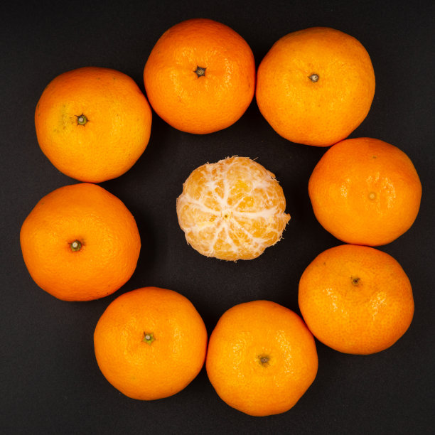特写:成熟的桔子排成一个圆圈，一个剥了皮的桔子在中间，孤立在黑色的背景上图片下载