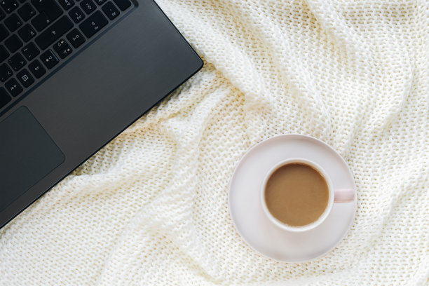 一杯咖啡放在白色的针织毯子上，还有一台笔记本电脑。在家工作，自由职业者的概念。俯视图，平躺图片下载