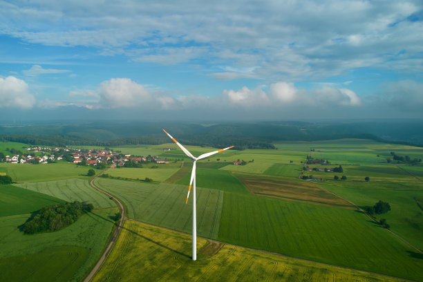 图片中央的农田上有一台风力涡轮机。通往德国斯瓦比亚白河上一个村庄的狭窄道路。蔚蓝的天空，乌云密布。鸟瞰图。图片下载
