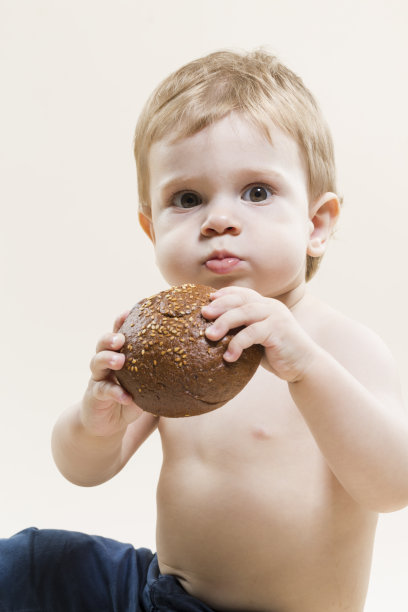 小男孩的肖像，手里拿着食物，吃着新鲜出炉的面包，在米色的背景下摆姿势。垂直的图像图片下载