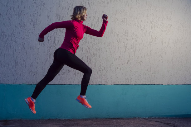 在水泥墙背景下集中进行户外慢跑训练的成熟女运动员。水平射图片下载