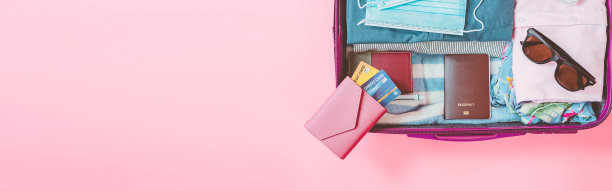 粉红色背景上有衣服和配件的手提箱包。伴随冠状病毒大流行的暑假旅行。网络横幅的尺寸。图片下载