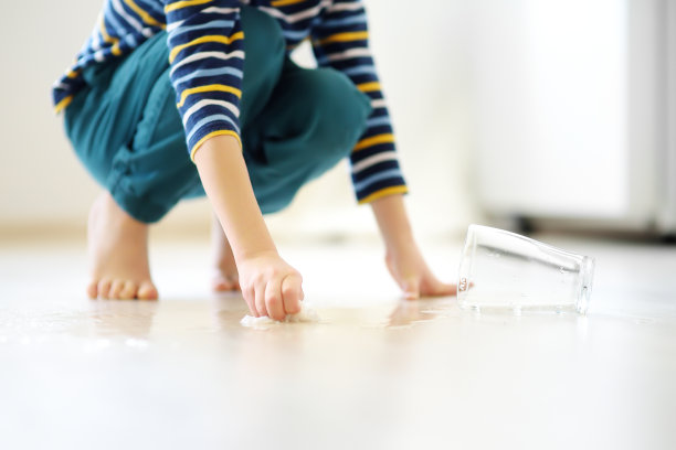 小男孩把玻璃杯里溅出来的水擦到地板上。教孩子自己打扫卫生。责任,准确性。图片下载