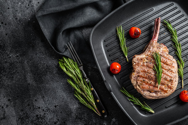 烤战斧肋眼牛肉(小牛肉)牛排在烧烤锅。黑色背景。前视图。本空间图片下载