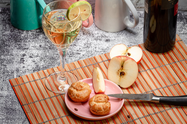一杯柠檬葡萄酒、一份闪电泡芙和厨房桌上的苹果片美食照片图片下载
