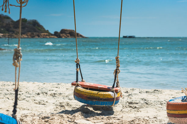 复制空间吊绳摆动旧轮胎漆橙蓝黄。自然沙滩明亮的海地平线地平线岛屿背景。白天阳光夏天欢乐乐趣。海洋天堂度假。美丽浪漫的风景图片下载
