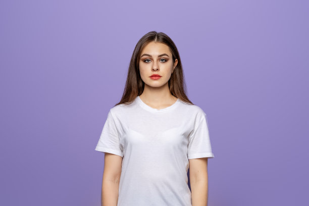 摄影棚拍摄的年轻女子，面带温柔的微笑，神情自信，身穿白色t恤，孤立地站在紫色的背景下图片下载