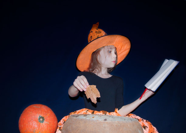 一个穿着女巫服装的女孩在大锅上变魔术。图片下载