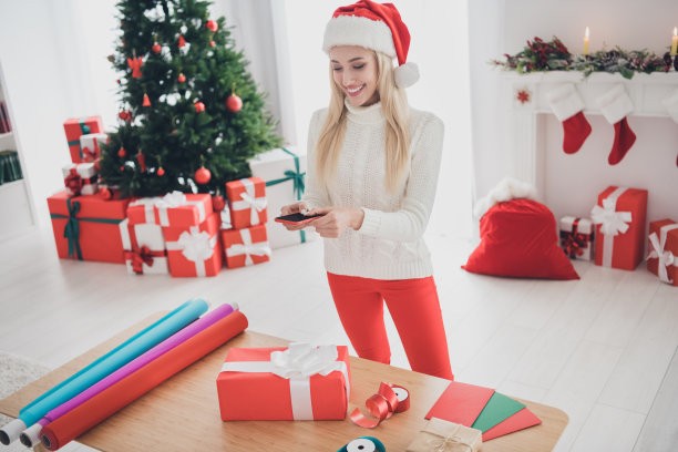 欢快快乐的年轻女人圣诞节照片，制作图片电话礼物包装材料圣诞节，在室内，在家里图片下载