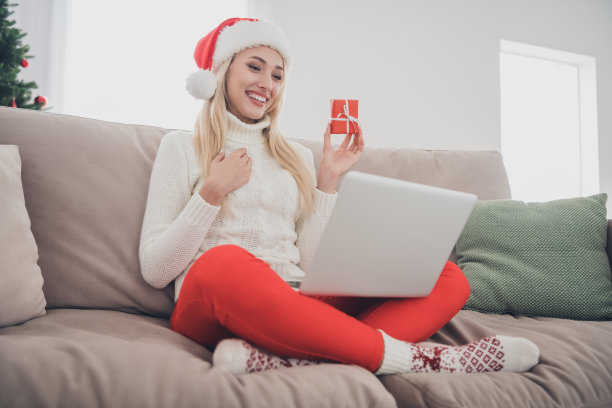欢快的年轻快乐女人的全身照片坐在沙发上，圣诞节聊天笔记本电脑，在屋里屋里装小礼物图片下载