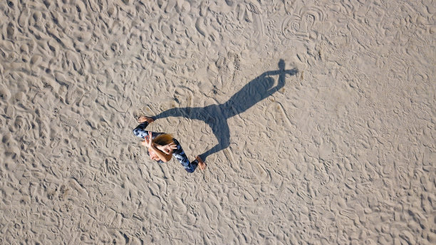 无人机观女子站在相扑瑜伽蹲姿的沙滩上，投下阴影图片下载