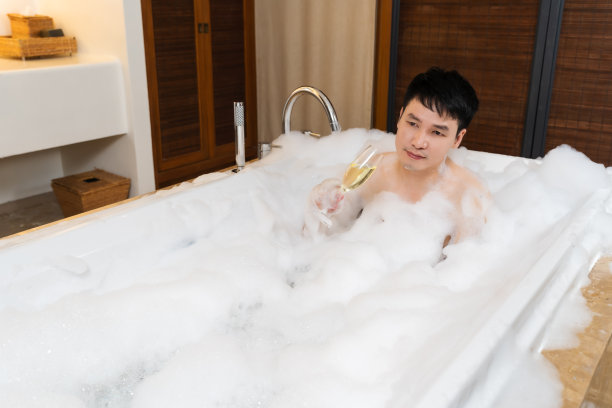 放松的男人一边喝着红酒，一边在浴缸里享受泡泡浴图片下载