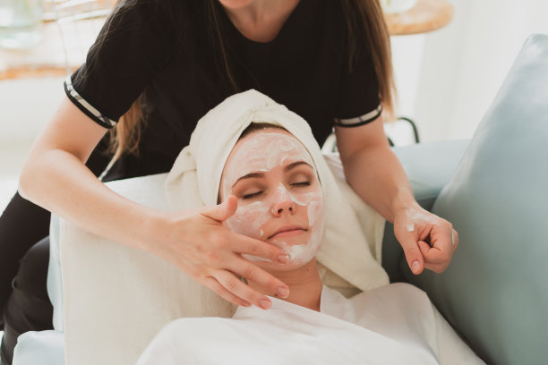 美容师为可爱的年轻女子做面部和按摩，用毛巾在她的头上图片下载