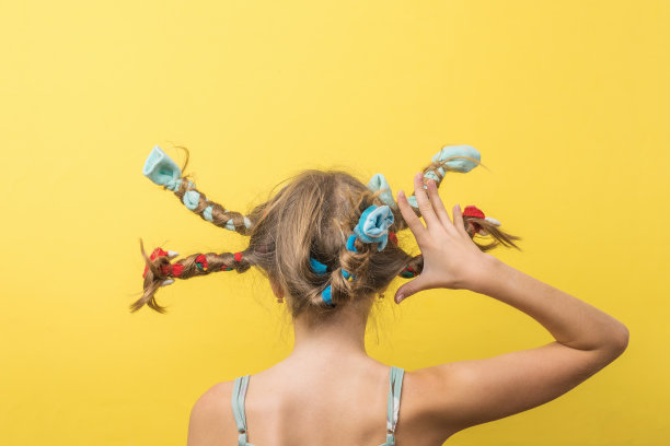 一个女孩抬起右臂，在黄色背景上编起飘飘的头发。着急。图片下载