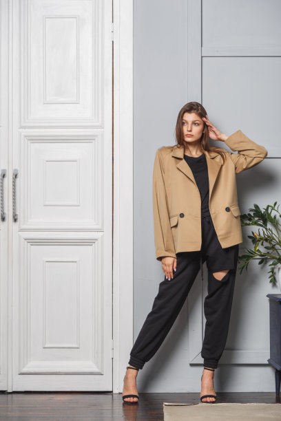 年轻的黑发女人穿着时髦的夹克和黑色的裤子。站在室内靠近门图片下载