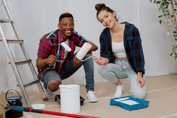两个相爱的年轻人正在装修他们的第一套公寓，他们跪在用纸板密封的地板上，从油漆托盘中舀起油漆，手里拿着滚轮图片下载