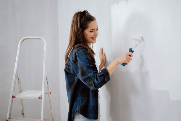 微笑美女装修公寓，手拿滚筒把墙壁刷成白色，搬家前最后的润色，做过油漆工、建筑师、装修师，业余时间画画图片下载