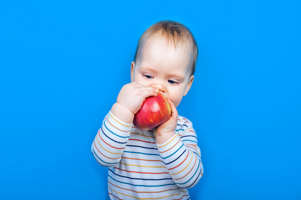 蓝色背景上有苹果的英俊男婴。健康饮食的概念和首先喂养的儿童，婴儿食品添加剂，过敏图片下载