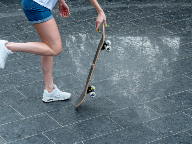 靠近照片的酷年轻女孩与美丽的腿在白色运动鞋滑板在闪亮的夏天。户外活动。街头文化。图片下载