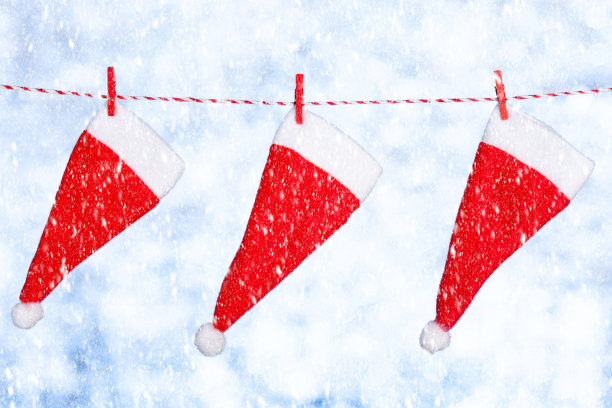 三顶红色的圣诞帽挂在一根绳子上，背景是模糊的闪亮的蓝灰色。副本的空间。概念图片下载