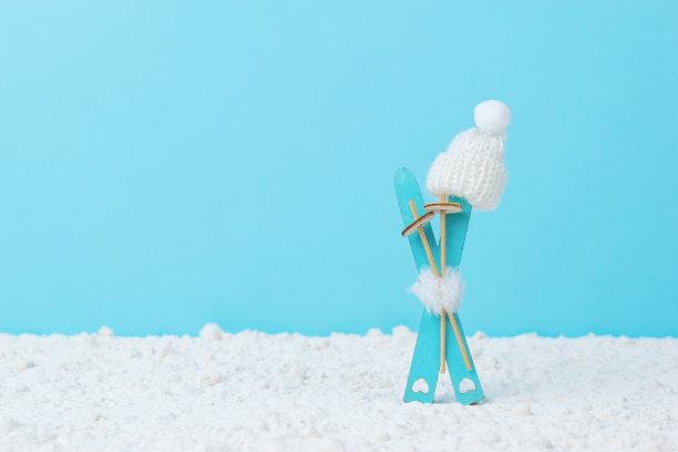 蓝色背景上的滑雪板被粘在雪地里，上面有树枝和一顶冬天戴的帽子。图片下载
