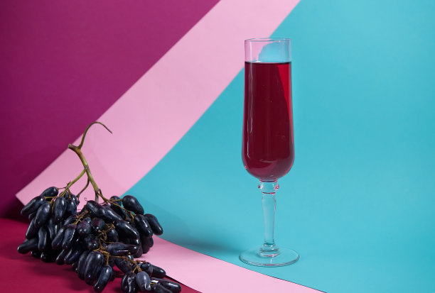 一杯漂亮的红酒在五彩斑斓的背景上，还有一串黑葡萄。以至上主义风格拍摄的照片。艺术在广告。酒单。优质的广告。本空间图片下载