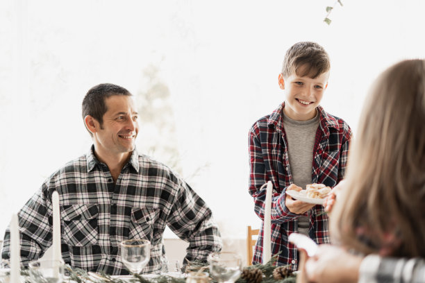 爸爸和孩子们坐在圣诞桌旁。家庭的圣诞早餐。女孩请哥哥吃蛋糕或纸杯蛋糕。概念新年在家。图片下载