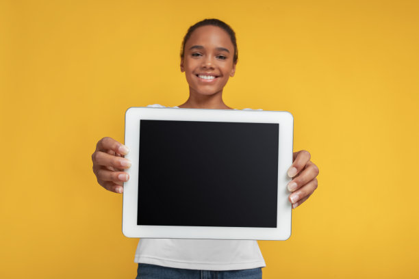 微笑的十几岁非洲裔美国女孩显示平板与空屏幕，孤立在黄色背景图片下载