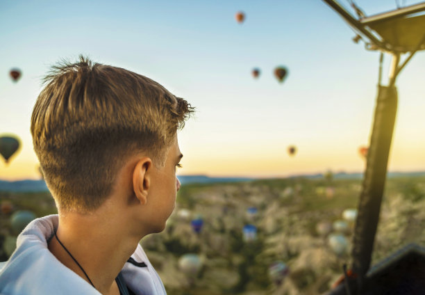 少年在热气球上观看日出，热气球在日出时飞越卡帕多西亚的童话风景丘陵，热气球。图片下载