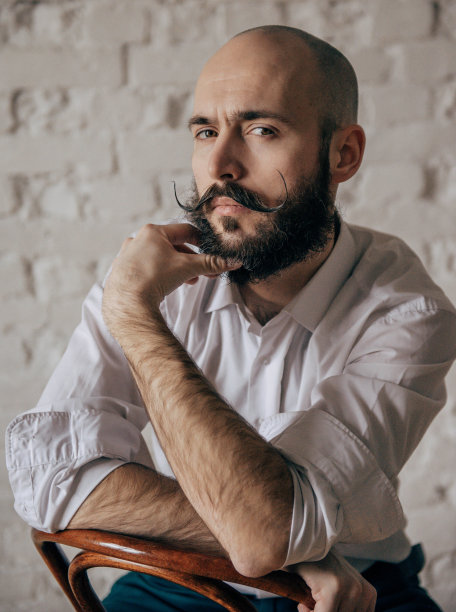 年轻的秃头留着胡子的男人穿着白衬衫坐在椅子上，肖像，图片下载