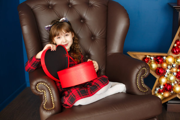 快乐的小女孩穿着红裙子在圣诞装饰中打开圣诞新年礼品盒图片下载