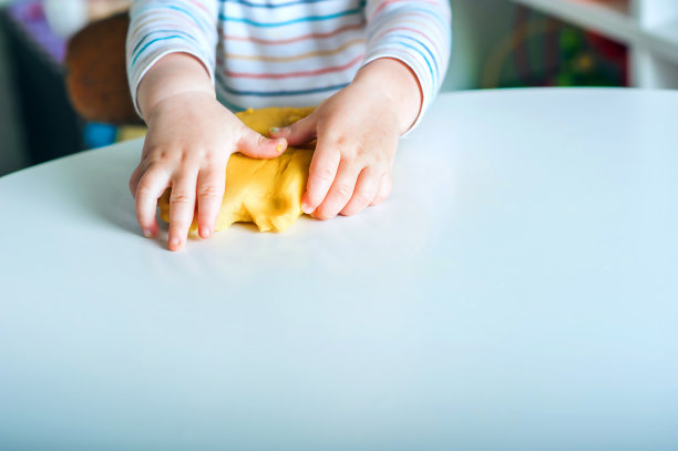 蹒跚学步的男孩在游戏室里玩黄色橡皮泥。图片下载