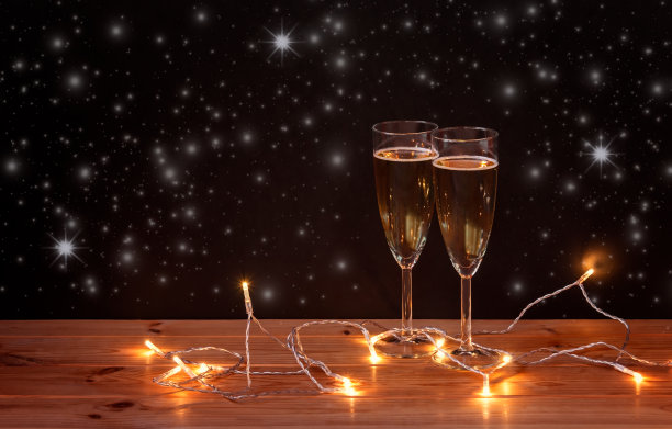香槟杯和黑暗背景下闪闪发光的圣诞彩灯。有选择性的重点。图片下载