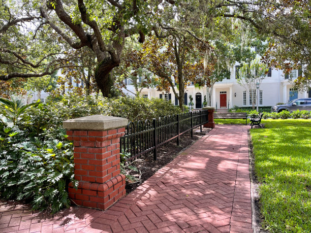 在佛罗里达州奥兰多的Celebration社区，一条红砖小路沿着公园，公园里有树木、金属围栏和木凳。图片下载