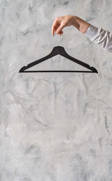 在阁楼里，粗糙的灰泥背景上有一只女性手和一个衣架。时尚设计师或购物者的极简主义概念。没有衣服穿，也没有商店卖。时尚博客横幅模板图片下载