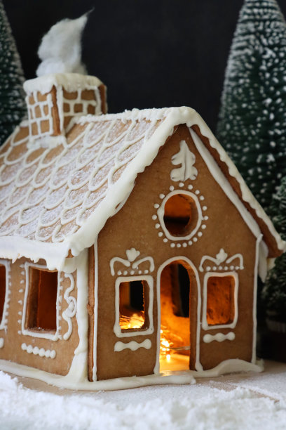 自制的特写图像，姜饼屋装饰白色皇家糖霜显示在雪天，夜间针叶林的场景，被仙女灯照亮，糖霜糖雪，黑色背景图片下载