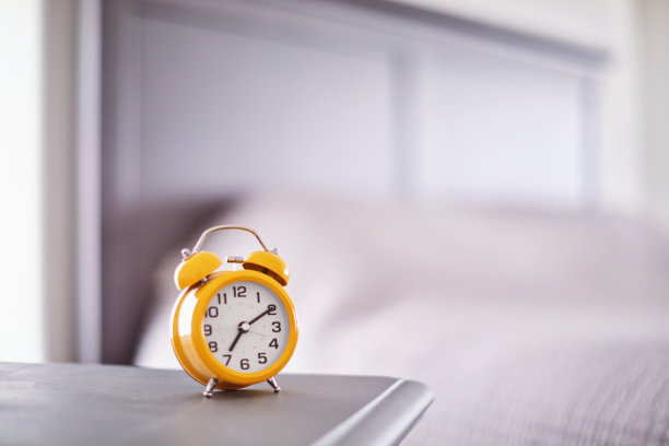 在现代明亮的卧室里，床头柜上的亮黄色闹钟图片下载