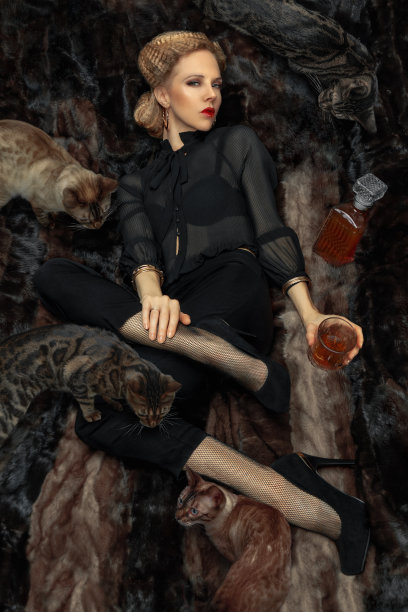 美丽的年轻迷人的金发女人躺在毛皮毯子上，手里拿着一杯酒，周围是孟加拉猫图片下载
