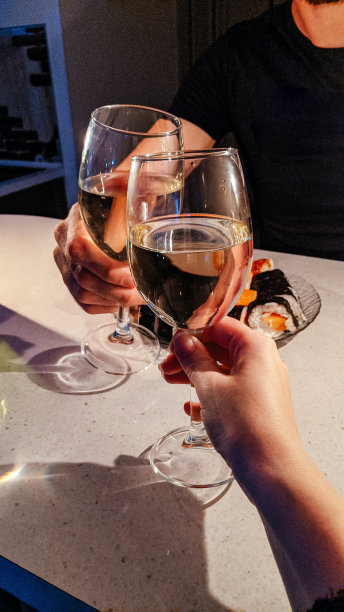 一个男人和一个女人的手碰杯喝白葡萄酒。浪漫的约会。图片下载