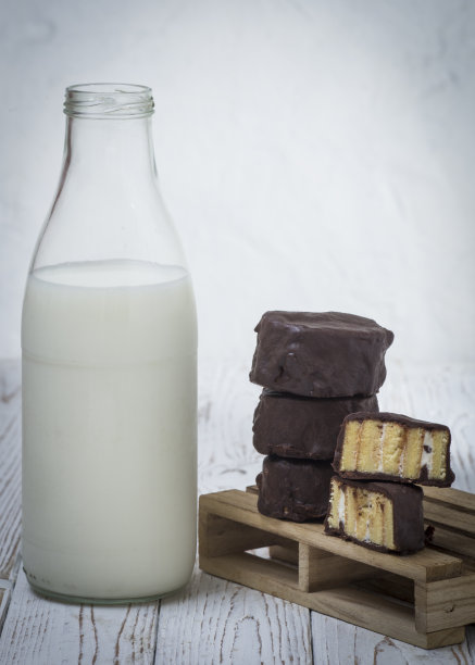 巧克力覆盖，奶油填充海绵蛋糕部分与一瓶牛奶在旁边。空间复制。文本空间图片下载