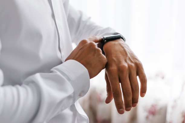 一个穿着白衬衫的商人，用着智能手表。男人的手收起来。图片下载