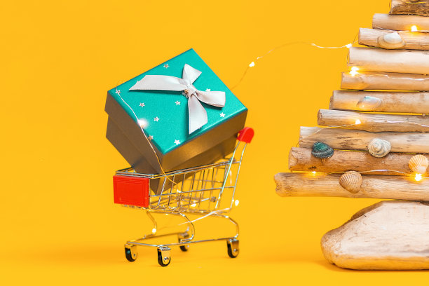 假日购物。一个玩具购物车和礼物，和一棵手工木制圣诞树。黄色背景。关闭了。圣诞节促销的概念图片下载