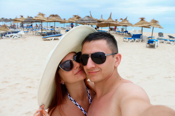 美丽的年轻情侣在雪白的海滩和大海的背景下自拍。图片下载