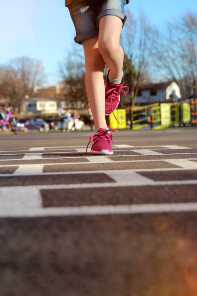一个女孩在户外操场上玩跳房子游戏图片下载